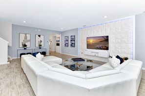 Uma sala de estar moderna com um sofá seccional, uma mesa de centro de vidro e uma TV de tela plana montada em uma parede texturizada.