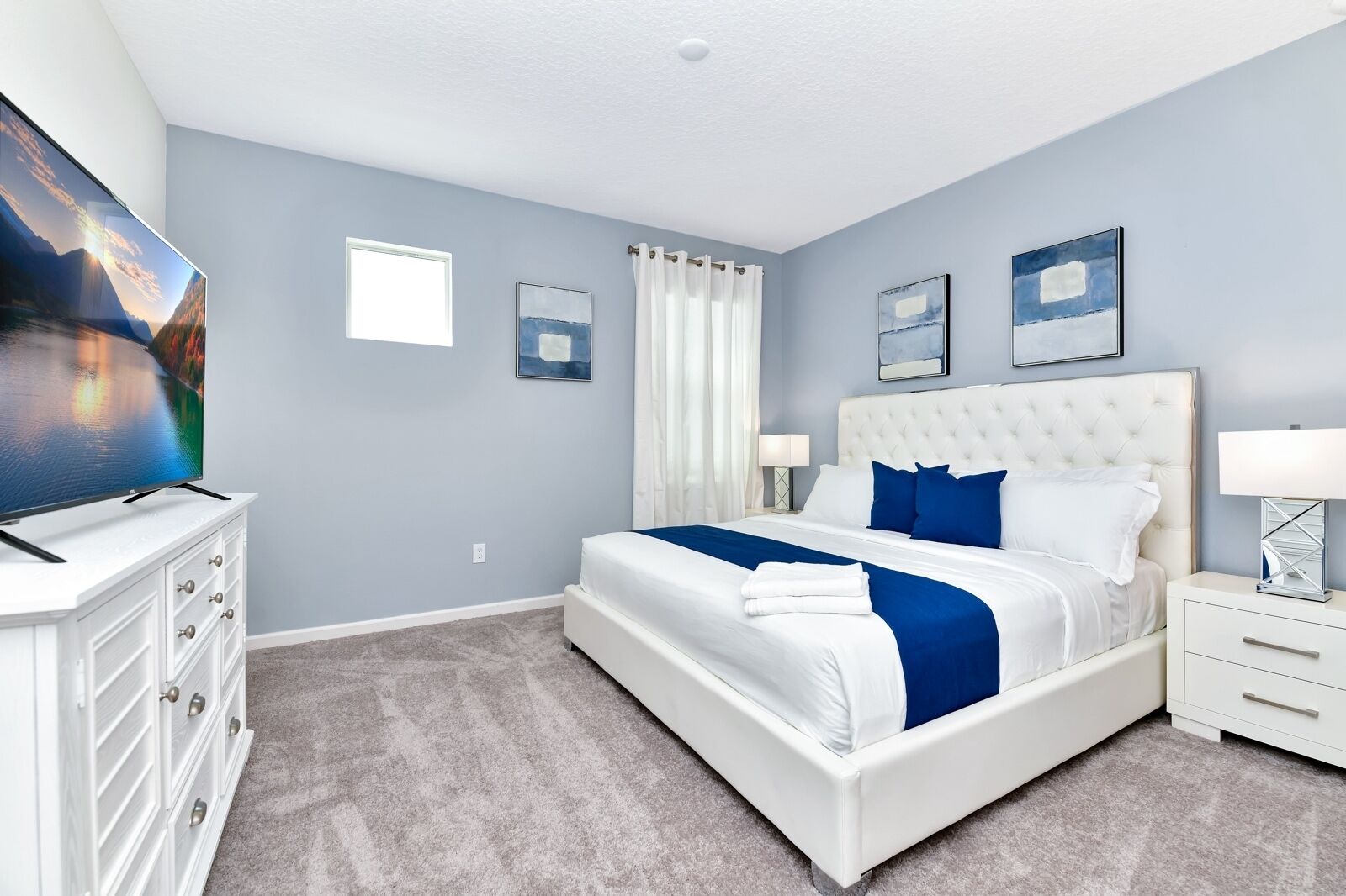 A modern bedroom with a large bed, a flat-screen TV, and a dresser.