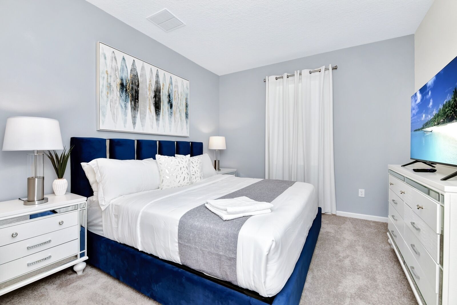 A modern bedroom with a large bed, a nightstand, a dresser, and a painting on the wall.