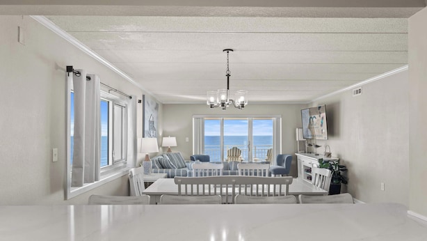 A spacious dining area with a large table, chairs, and a view of the ocean through large windows. - Salty Sands 2 301 | Oceanfront w/ Balcony & Views (Ocean City)