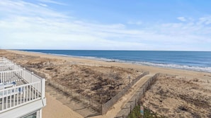 A beach view with a white building, sandy dunes, and a wooden fence. - Salty Sands 2 301 | Oceanfront w/ Balcony & Views (Ocean City)