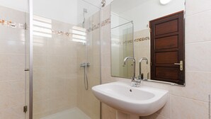 A bathroom with a glass shower enclosure, a white sink, and a wooden door. - Studio 102 - Le Balisier (Les Trois-Îlets)