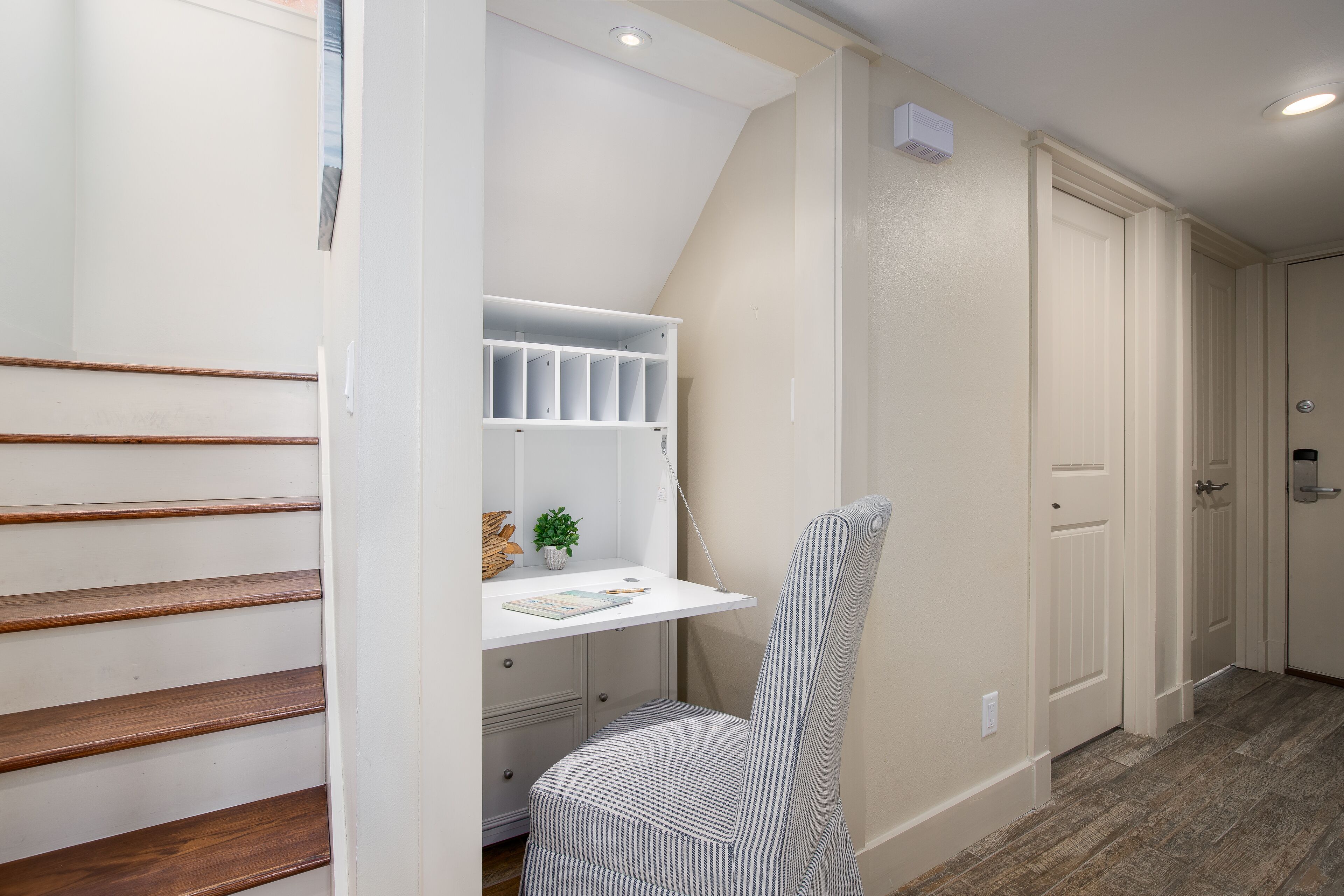A staircase with wooden steps, a white desk with storage, and a striped chair.