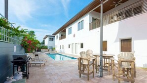 A modern outdoor pool area with lounge chairs and a barbecue setup.