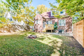 A backyard with a wooden deck, a fire pit, and a brick house. - Walk To Aggieville from Brick Cottage with Man Cave, Shuffle Board, Back Yard (Manhattan)
