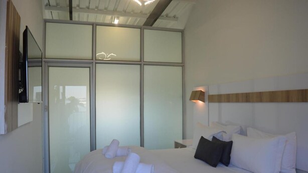 Una habitación de hotel moderna con una cama grande, un televisor de pantalla plana montado en la pared y un ventanal corredero que da a un balcón.