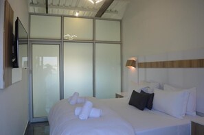 A modern hotel room with a large bed, a flat-screen TV mounted on the wall, and a sliding glass door leading to a balcony. - Dream Sleep (East London)