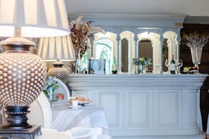 Un coin repas avec une table blanche dressée pour deux personnes, une lampe décorative et une cheminée surmontée d’un miroir.