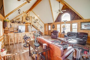 Un ampio loft con soffitto alto, travi in legno, angolo cottura, soggiorno con mobili in pelle e una scala che conduce a un livello superiore.