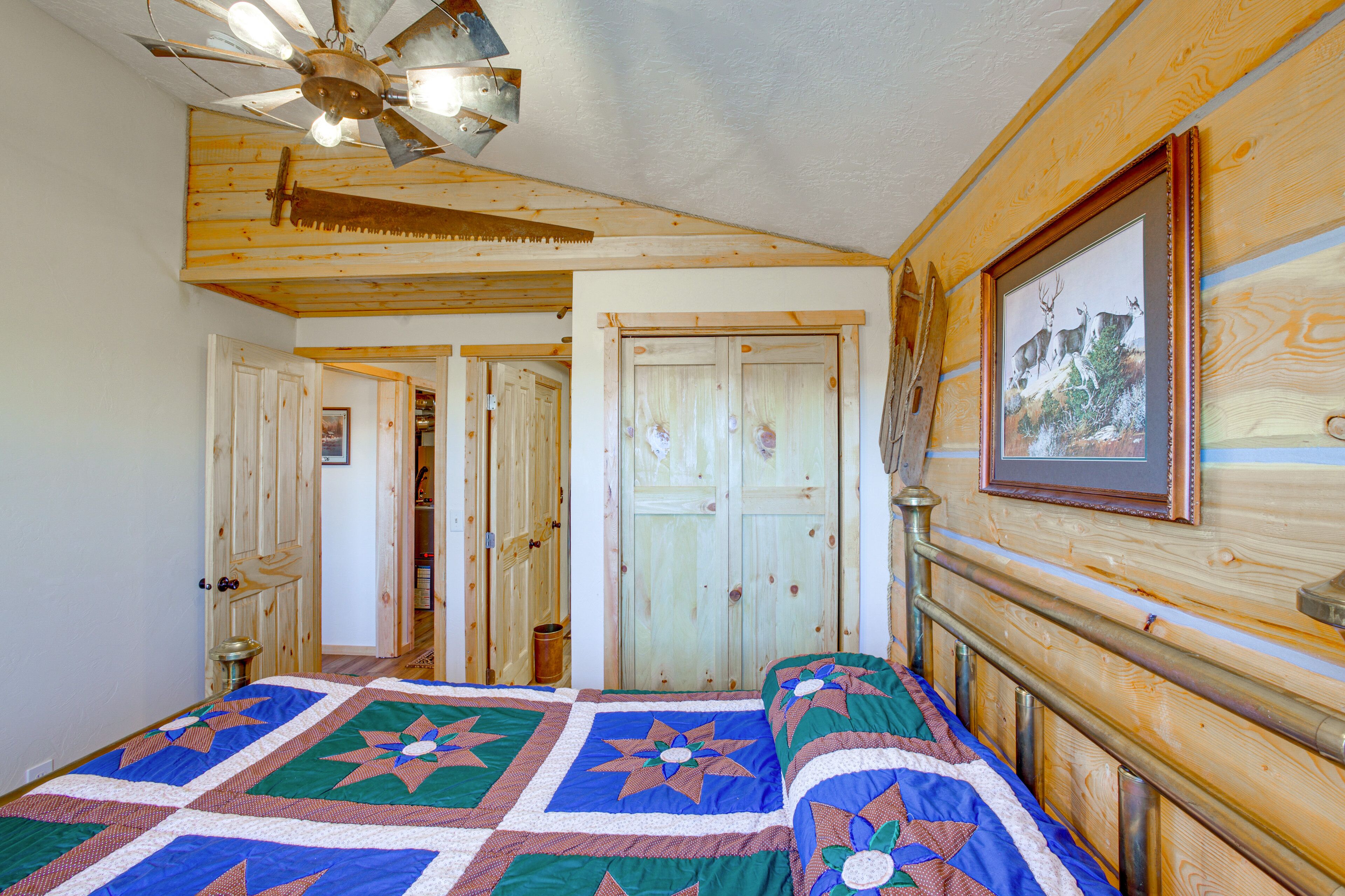 Quarto com teto de madeira, ventilador de teto, cama com colcha e quadro na parede.