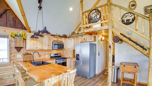 A rustic kitchen with wooden cabinets, a stainless steel refrigerator, and a wooden island with bar stools. - Roberts Home w/ Western Decor & Mountain Views! (Roberts)