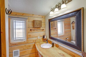 Bagno di una baita in legno con uno specchio grande, una finestra e un lavandino.