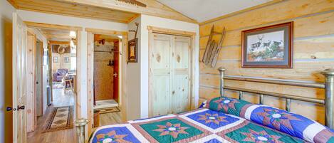 Une chambre dans une cabane en bois, avec un lit, un ventilateur de plafond et un tableau encadré au mur.