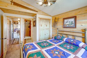 A wooden cabin bedroom with a bed, a ceiling fan, and a framed picture on the wall. - Roberts Home w/ Western Decor & Mountain Views! (Roberts)