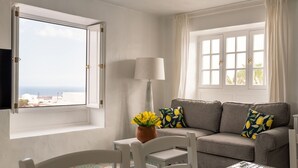 Et hyggeligt værelse med sofa, bord, stol, lampe og havudsigt.