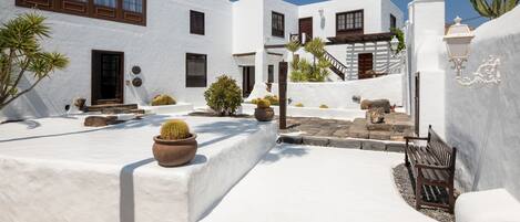A white-walled building with a courtyard, featuring a cactus, a bench, and a staircase.