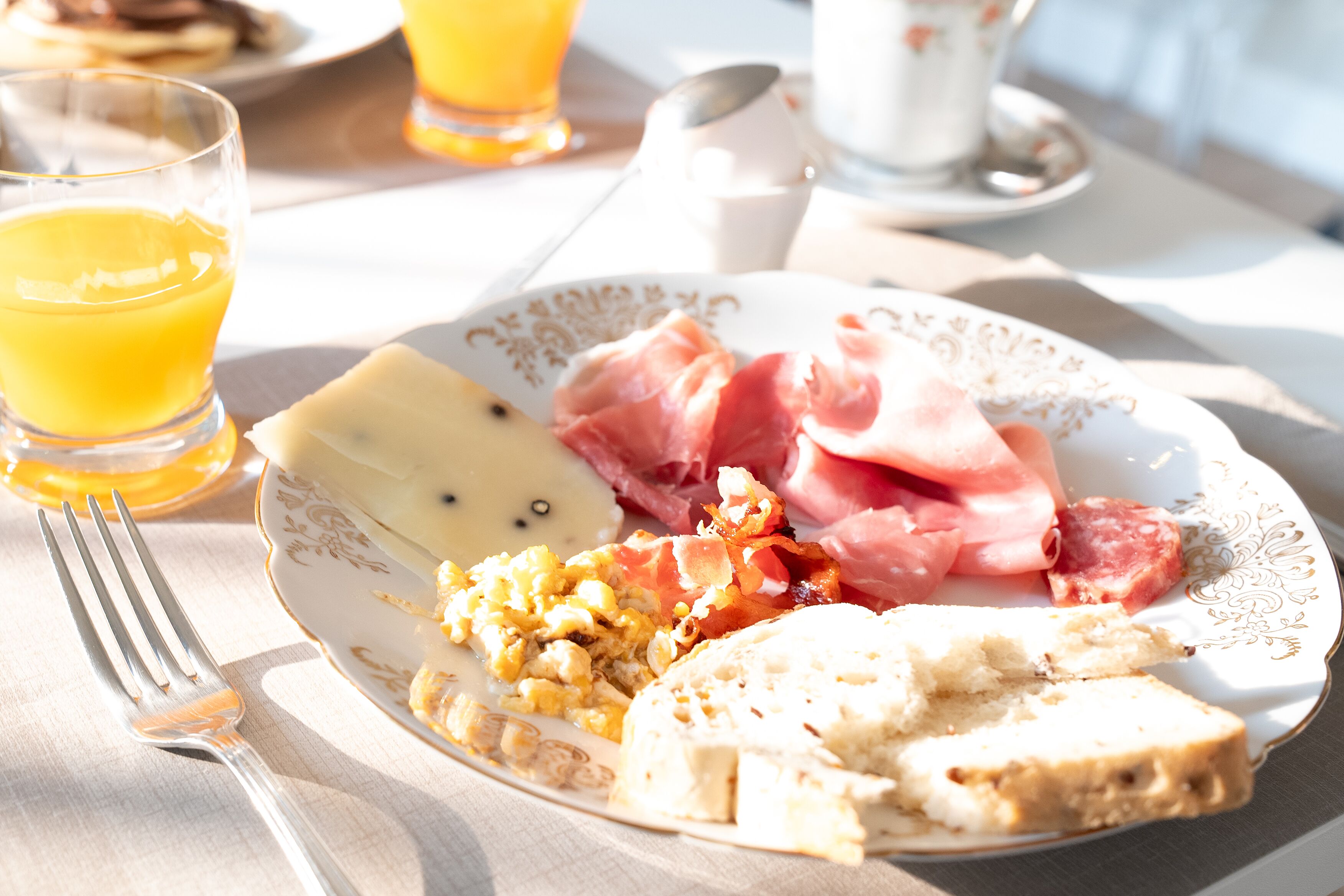Un plato de desayuno con huevos, jamón y tostadas sobre una mesa, junto a un vaso de jugo de naranja.