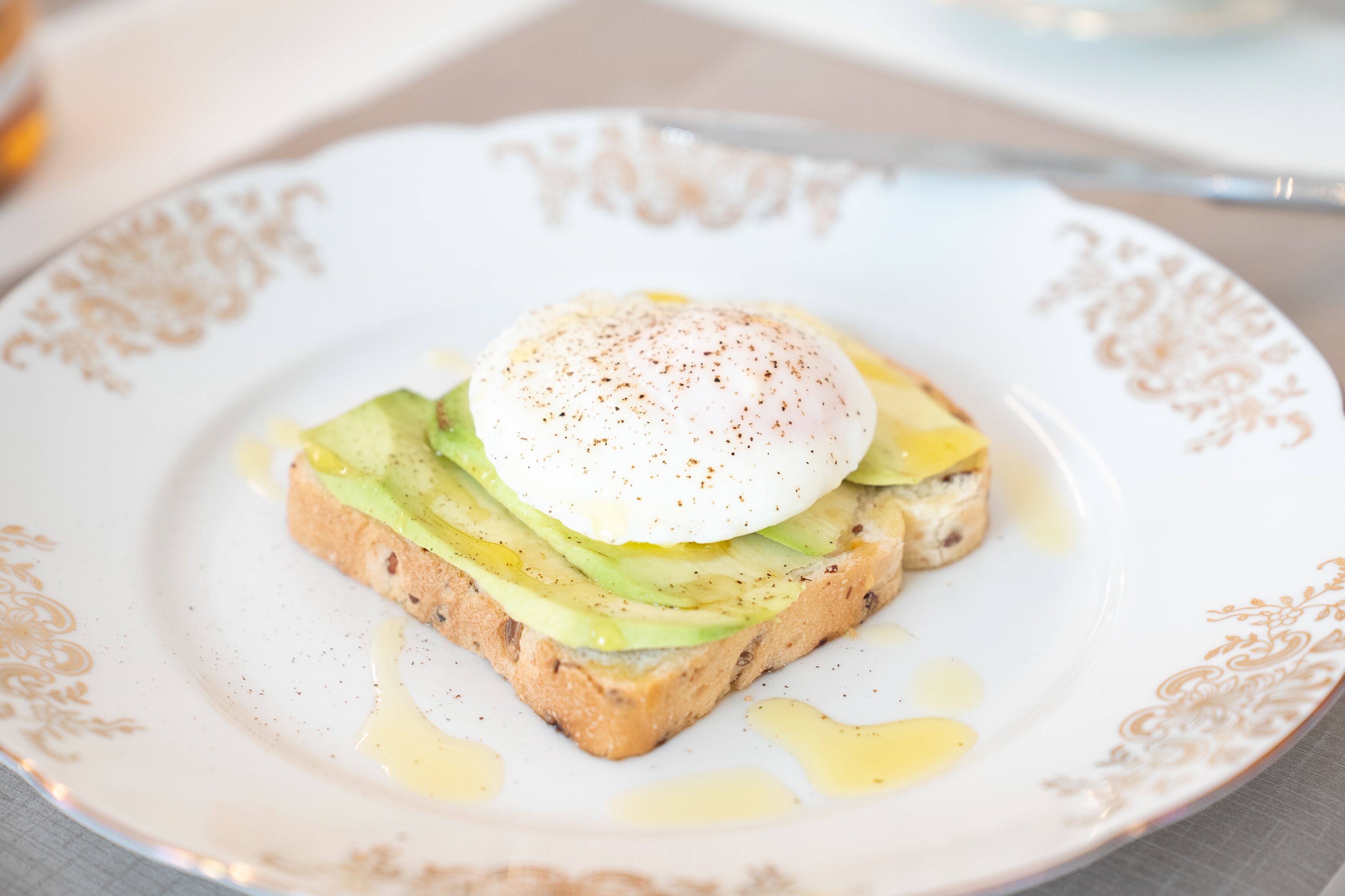 En tallrik med rostat bröd, toppad med avokadoskivor och ett pocherat ägg, serverad på en vit tallrik med en dekorativ kant.