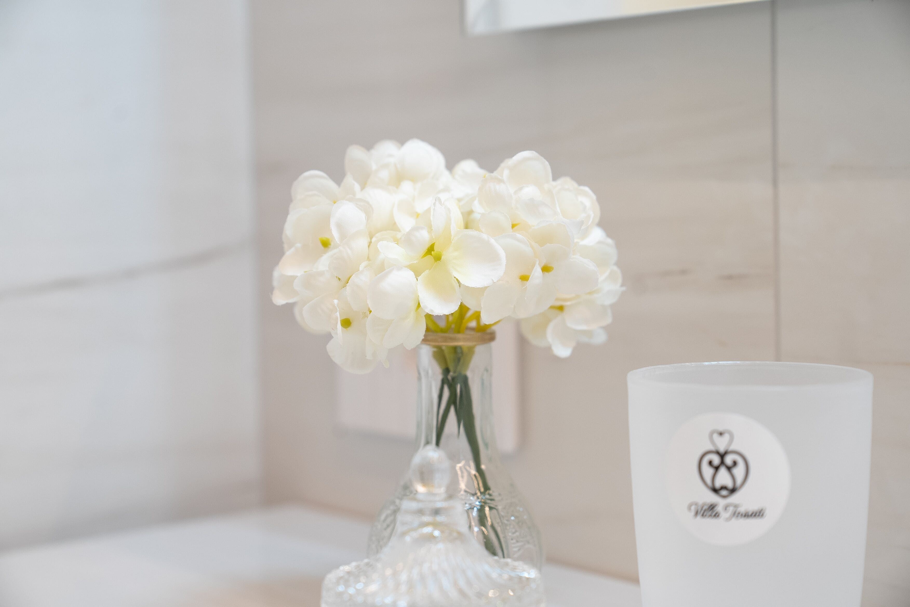 Un vase en verre transparent contenant des fleurs blanches et un chandelier blanc orné d’un logo.