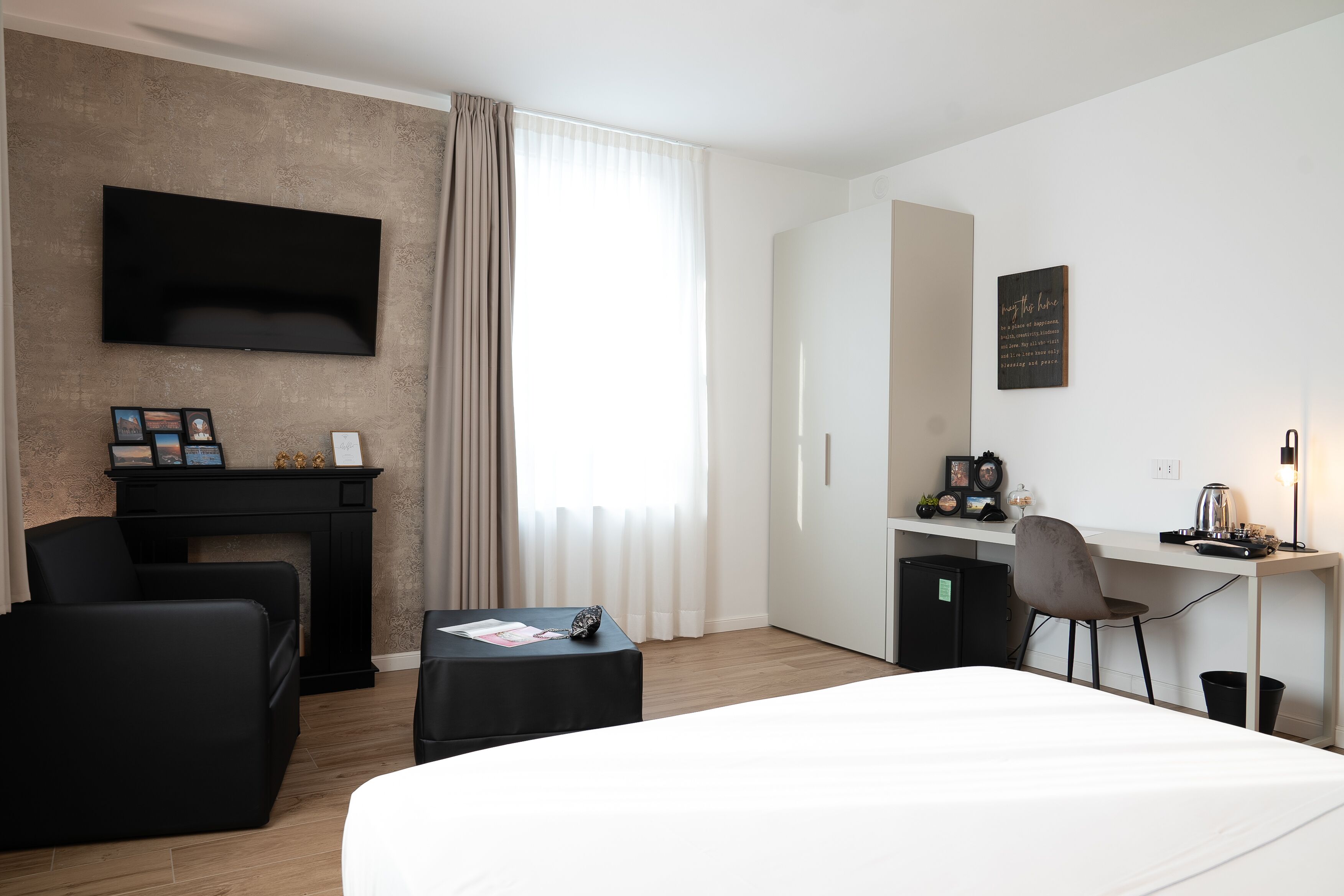 Moderni hotellihuone, jossa on suuri sänky, työpöytä tuolilla, seinälle asennettu taulutelevisio, takka ja ikkuna, jossa on verhot.