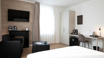 Moderni hotellihuone, jossa on suuri sänky, työpöytä tuolilla, seinälle asennettu taulutelevisio, takka ja ikkuna, jossa on verhot.