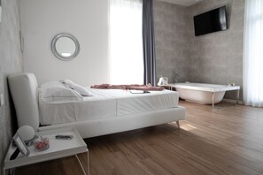 Un dormitorio moderno con una cama grande, una mesita de noche con lámpara, un espejo, un televisor en la pared y un baño con bañera.