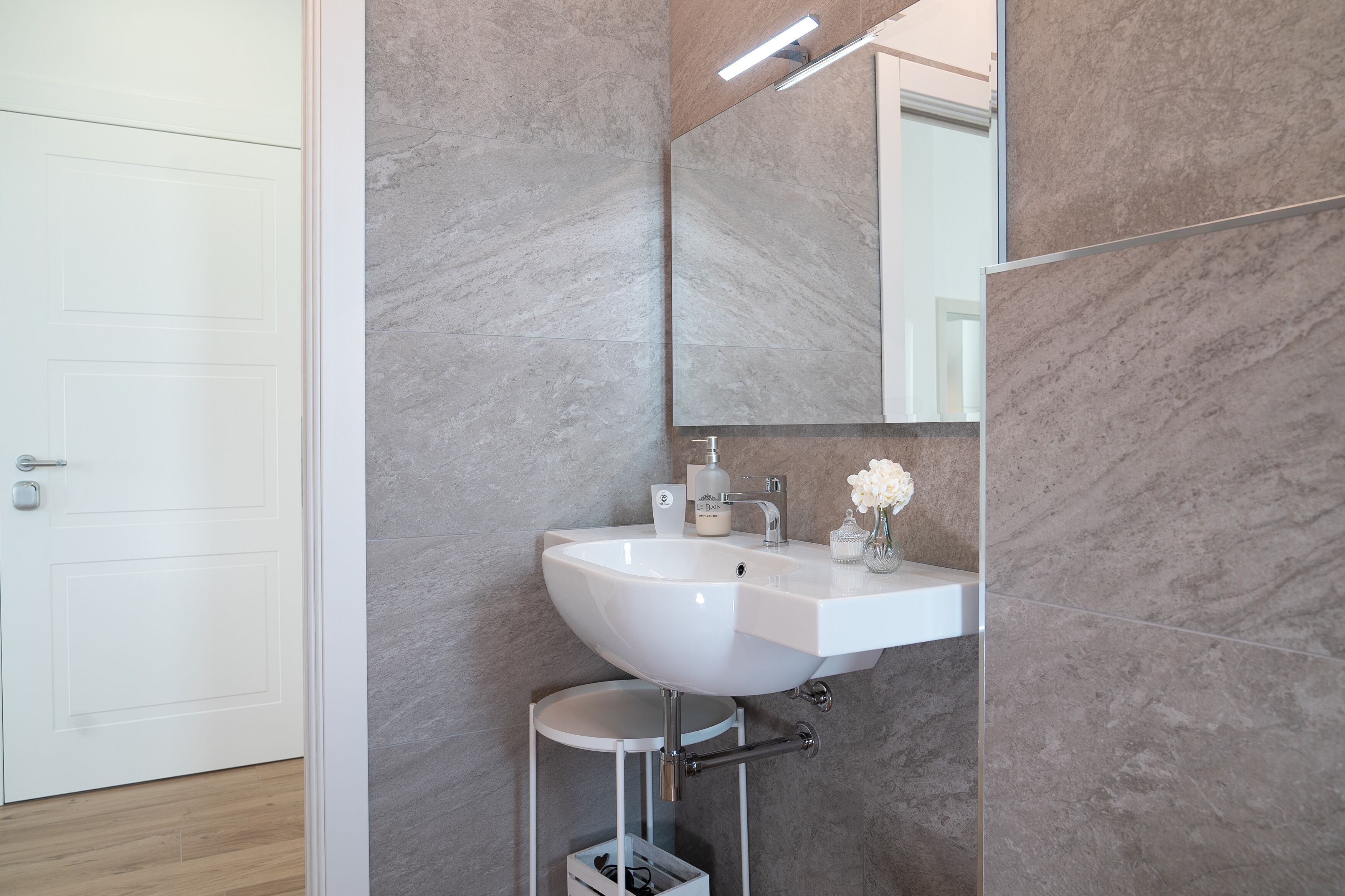 A modern bathroom with a white sink, mirror, and marble walls.