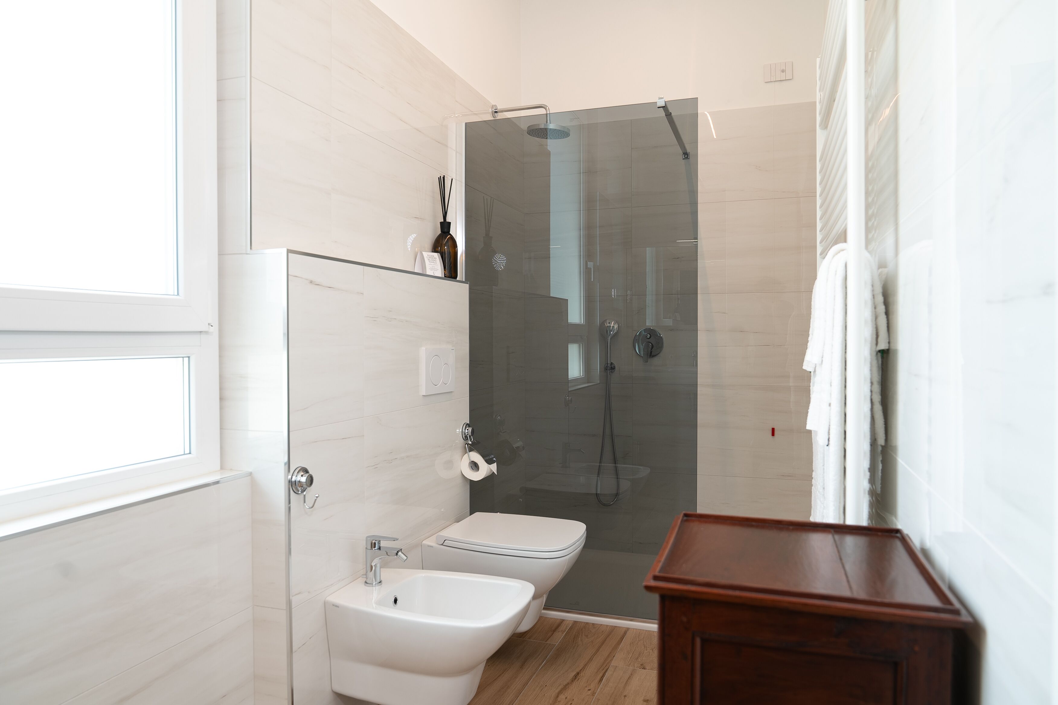 Un baño moderno con ducha de vidrio, inodoro blanco, bidet y tocador de madera.