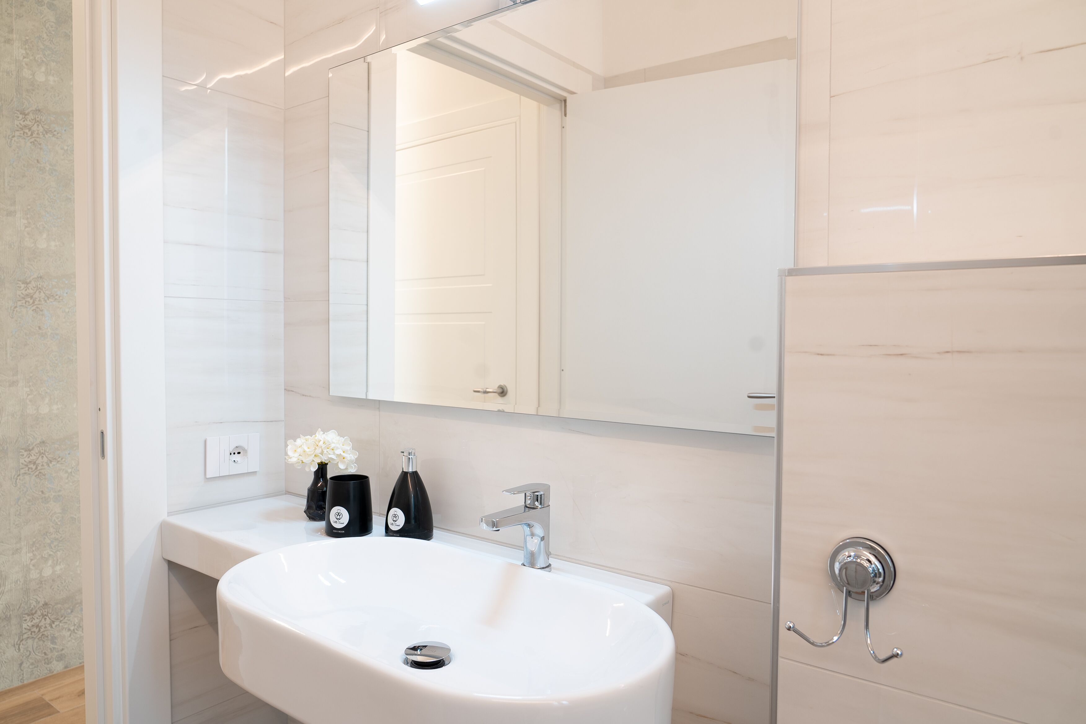 Un baño moderno con un lavamanos blanco, un espejo y un perchero para toallas.