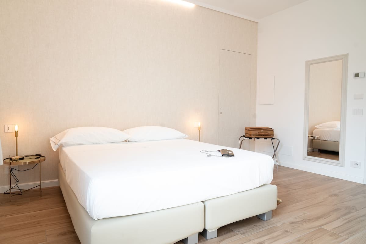 A bedroom with a large bed, bedside tables, a mirror, and a suitcase.