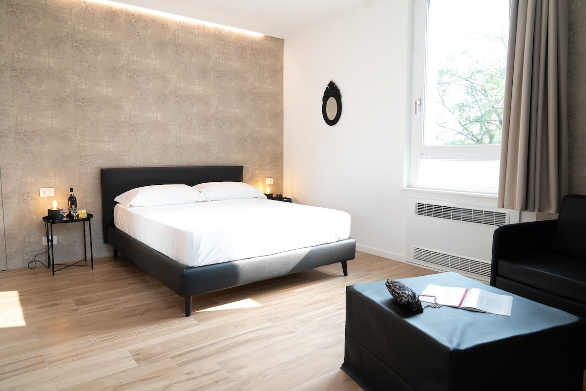 A modern bedroom with a large bed, bedside lamps, a small table, and a window with curtains.