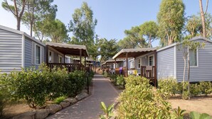 A row of mobile homes with a paved walkway between them, surrounded by greenery and trees.