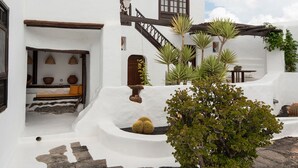 A white-washed building with a staircase leading to a door, surrounded by potted plants and cacti. - Las Pergolas Villa Rural - Apartamento Yaiza (Tías)