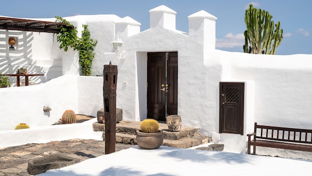 A white-washed building with a dark wooden door, a bench, and cacti in the foreground. - Las Pergolas Villa Rural - Apartamento Yaiza (Tías)