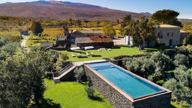 Ein Pool mit einer Steinterrasse und einer Treppe, die zu einer Terrasse führt, mit Blick auf einen Berg im Hintergrund.