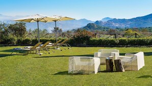 Ein Außenbereich mit Lounge-Möbeln und Sonnenschirmen, einer Rasenfläche und einem malerischen Bergblick.