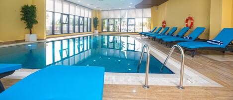 An indoor swimming pool with blue lounge chairs and a lifebuoy on the wall.