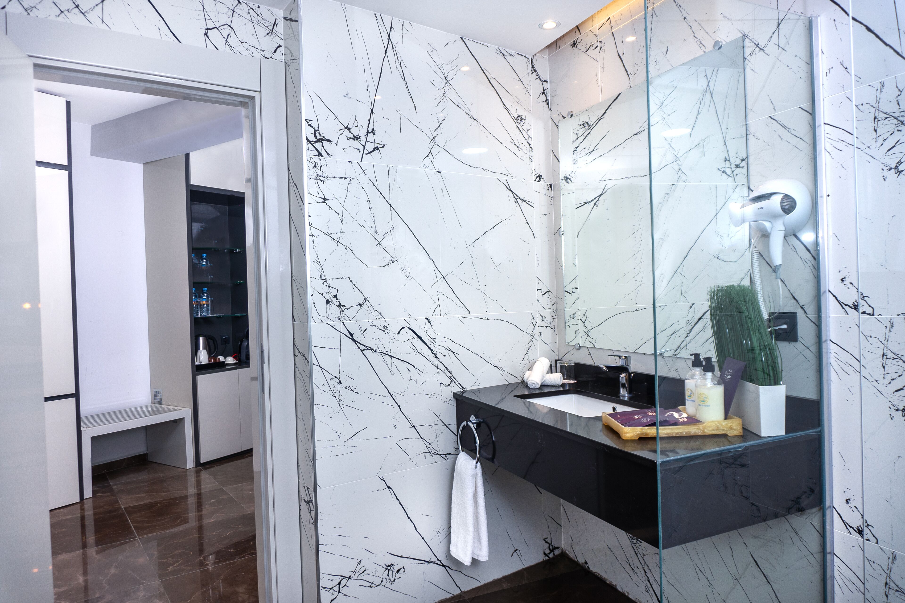 A modern bathroom with a marble backsplash, a glass shower enclosure, and a black countertop with toiletries.
