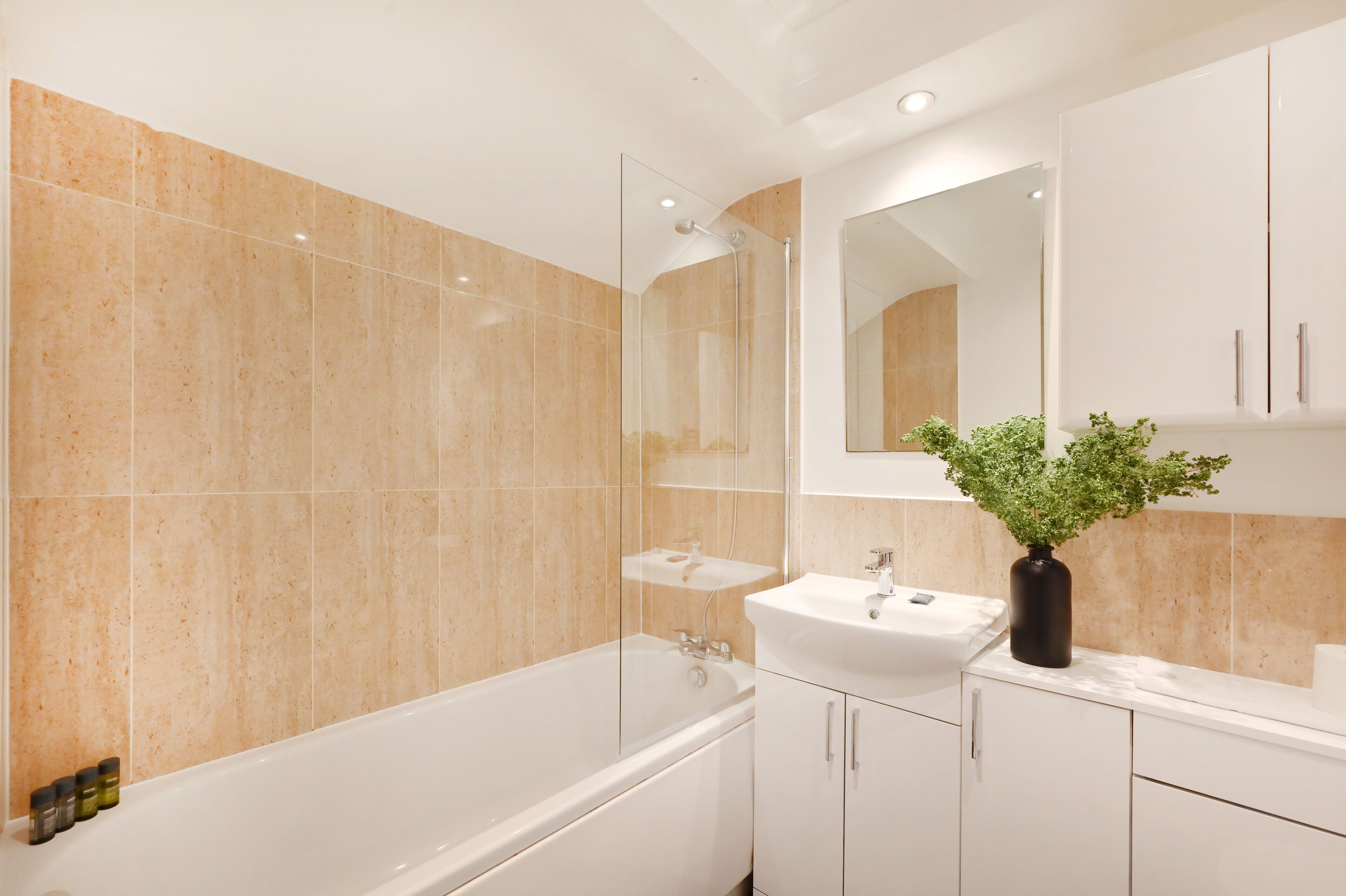 Un baño moderno con ducha de vidrio, lavamanos blanco y espejo sobre él.