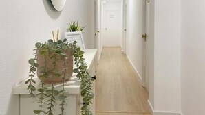A hallway with a white wall, a wooden floor, a white cabinet with a mirror, and a potted plant. - Hostal Sol (Zamora)