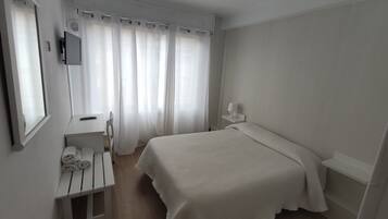 Un dormitorio con cama, un escritorio con silla, un espejo y una ventana con cortinas.