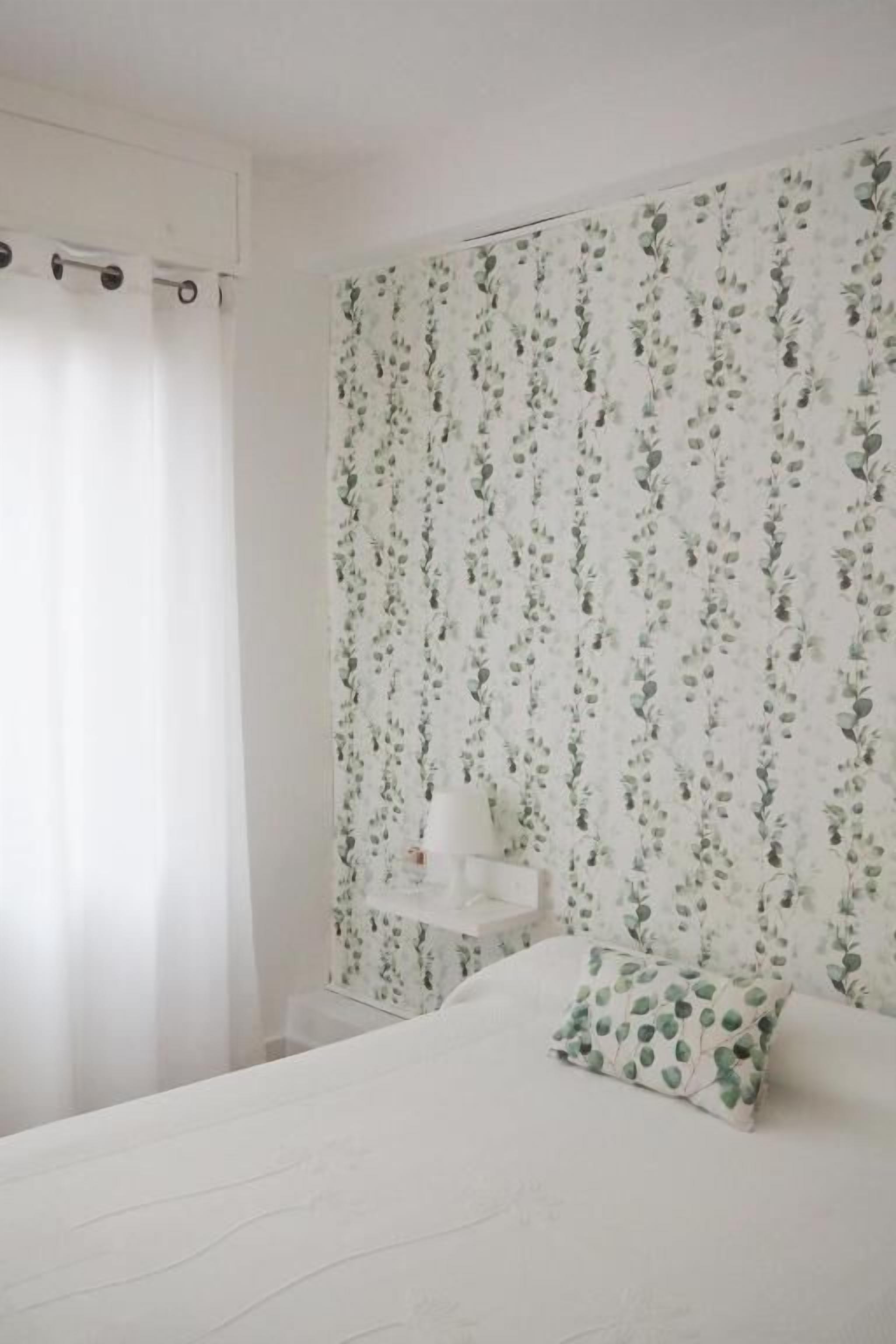 A bedroom with a bed, a nightstand, and a wall with floral wallpaper.