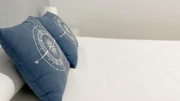 Quarto com uma cama branca, dois travesseiros azuis com desenho branco e três mesas de cabeceira brancas com objetos pequenos.