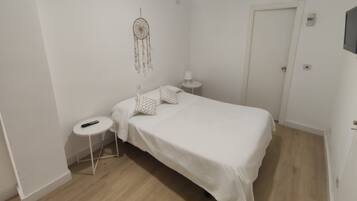 Une chambre à coucher minimaliste, avec un lit simple, une table de chevet, une petite table ronde et un attrape-rêves accroché au mur.