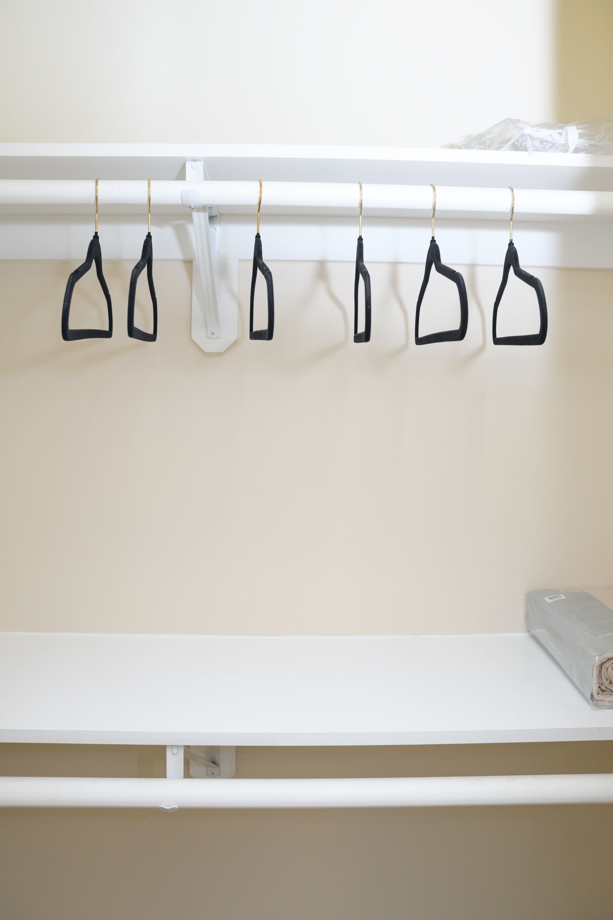 A white closet with black hangers and a rolled-up towel on the shelf.