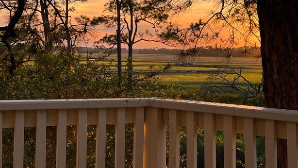 Uitzicht vanaf een balkon met een balustrade, over een landschap met bomen en velden tijdens de zonsondergang.