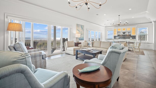 A spacious living room with a large window, a chandelier, and a view of the ocean. - Luxury Oceanfront Retreat | 6 Ensuite Bedrooms | Sleeps 14 | Golf Cart Included | Steps to Beach Club (Fripp Island)