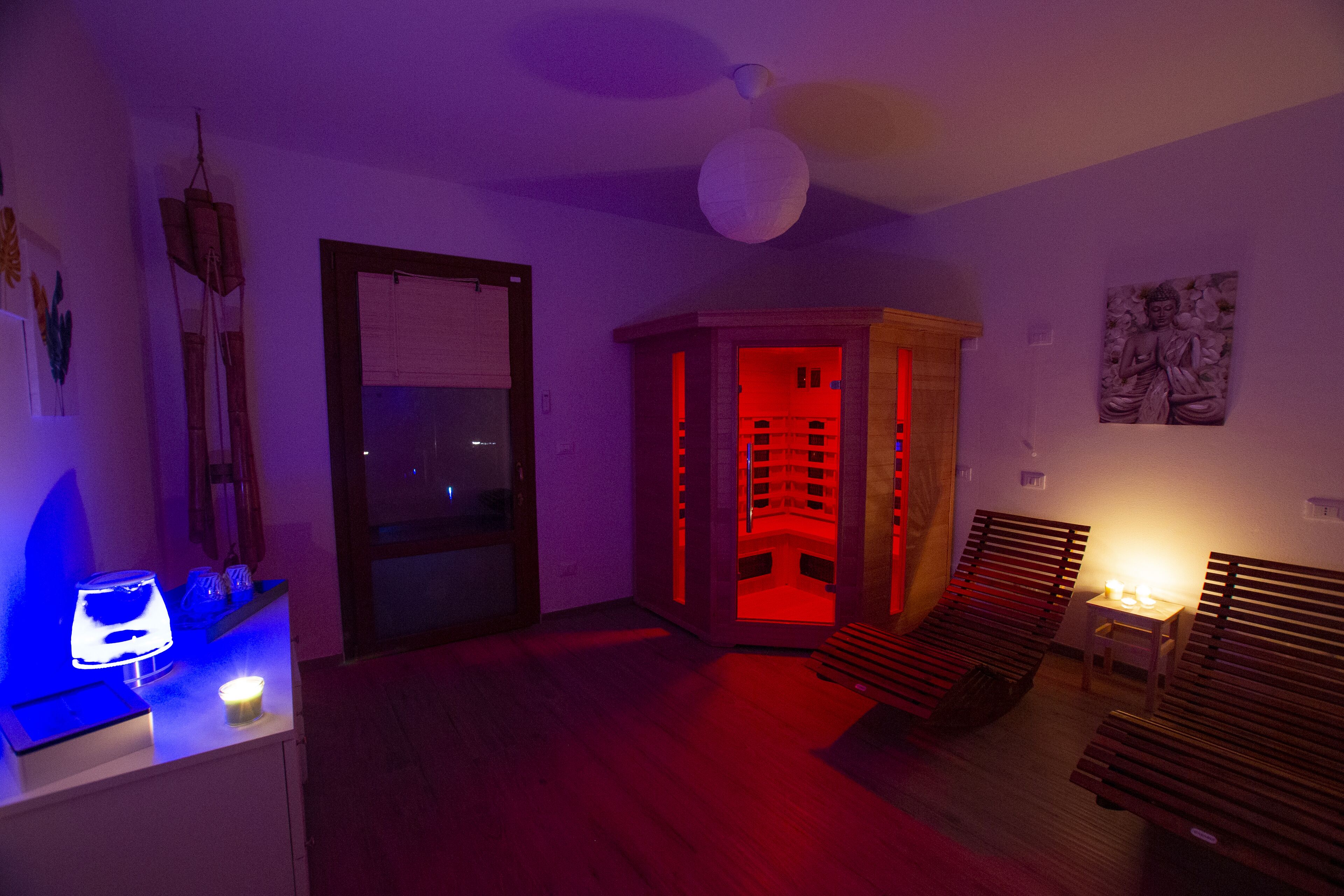 Una habitación con un banco de madera, una mesita con una lámpara y una esquina iluminada con luz roja.