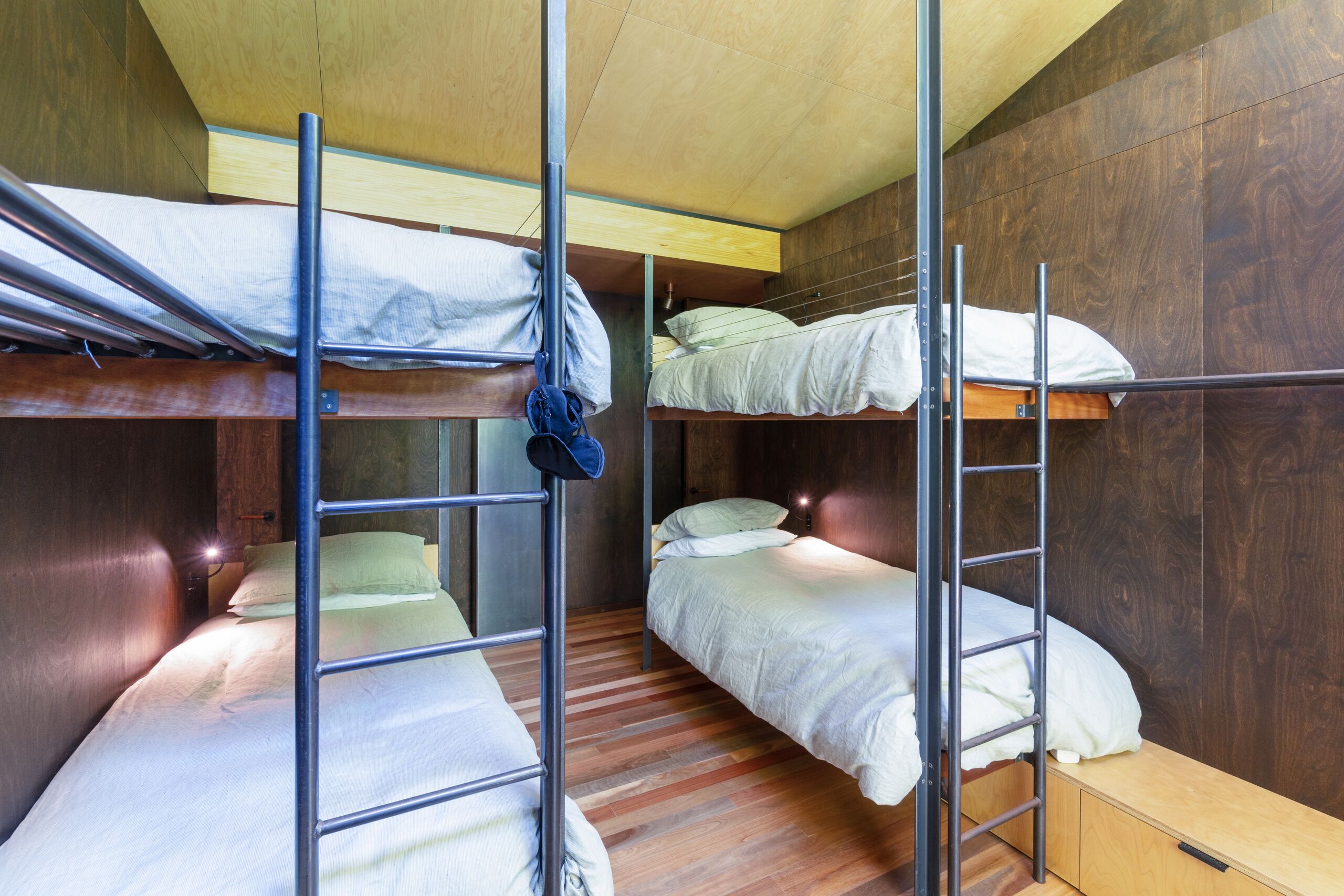 A dormitory room with bunk beds, wooden flooring, and a wooden wall.