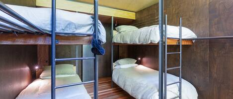 A dormitory room with bunk beds, wooden flooring, and a wooden wall.